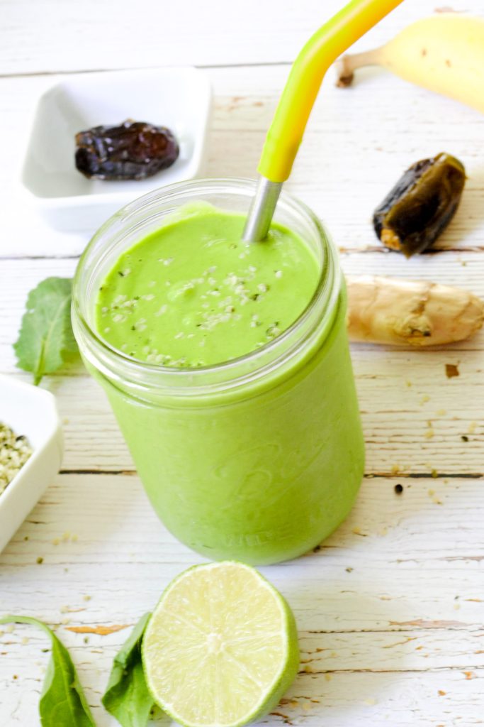 A vibrant green smoothie in a glass cup with metal straw.