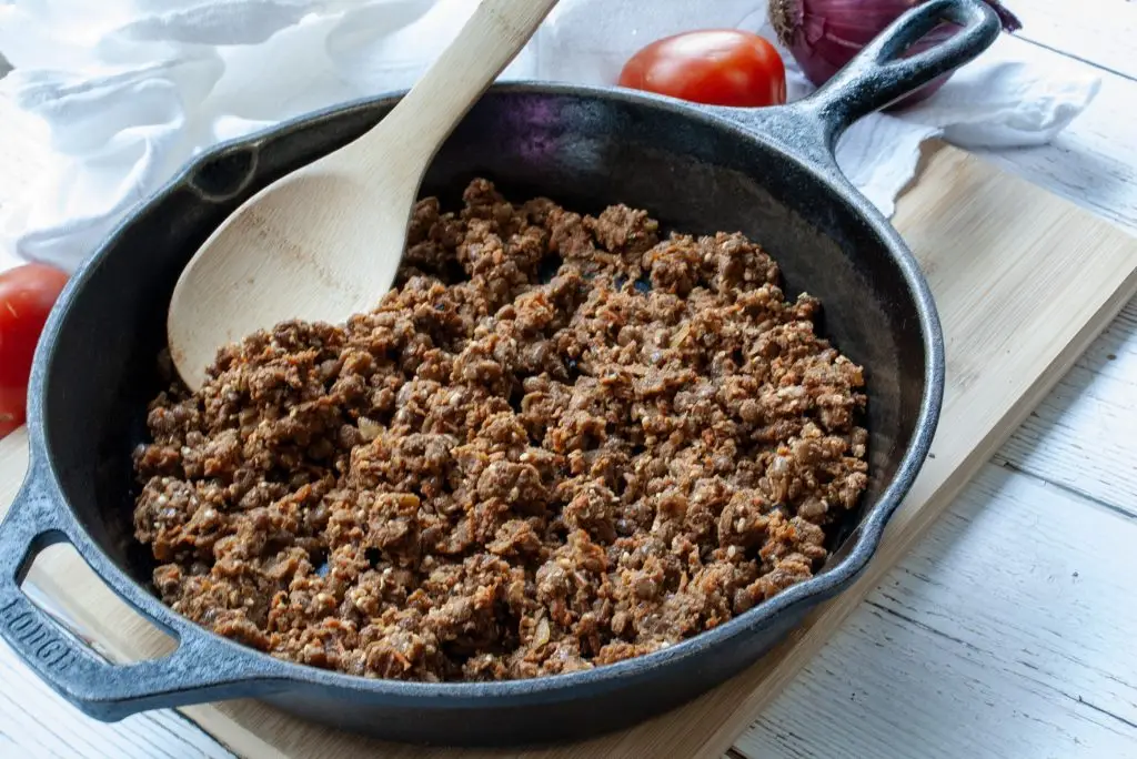 A cast iron pan filled with Easy Vegan Taco Meat and a wooden spoon.