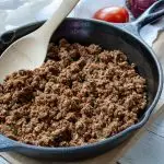 A cast iron pan filled with Easy Vegan Taco Meat and a wooden spoon.