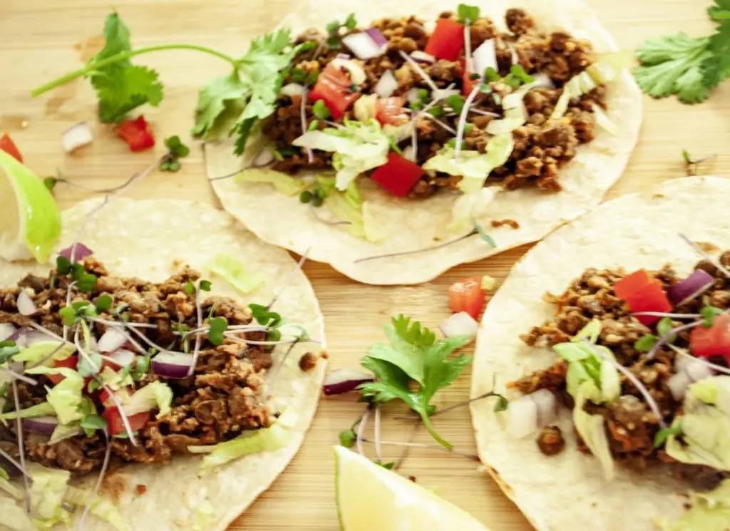 3 tacos on a platter with Easy Vegan Taco Meat, lettuce, tomato and microgreens