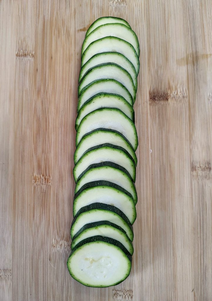 A row of neatly sliced zucchinis on a wooden cutting board.