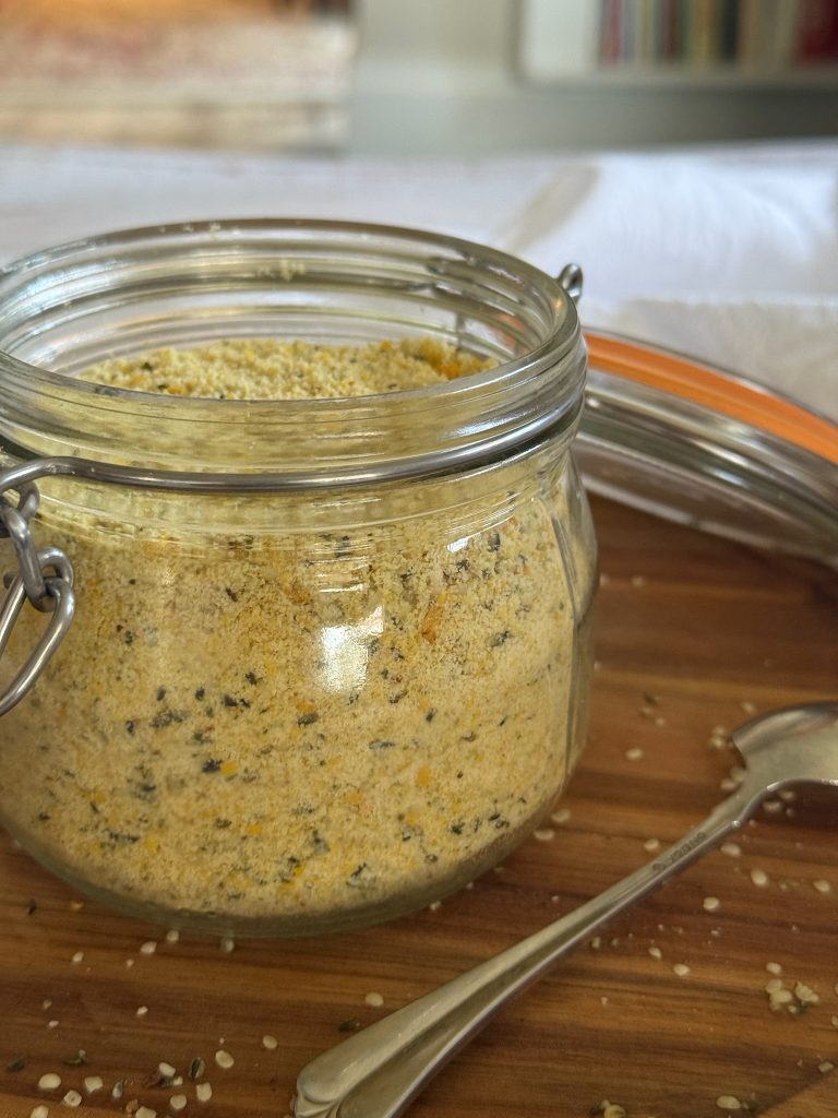 An open glass jar of vegan parmesan on a wooden table.