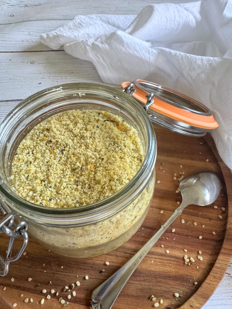 A mason jar filled with vegan parmesan cheese on a round wooden board.